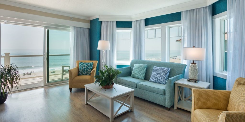 an oceanfront room decorated with a blue sofa, tan armchair and light wooden coffee table