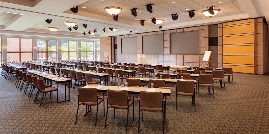 a large and open conference room with tables and chairs set up in classroom style seating facing a moderator post