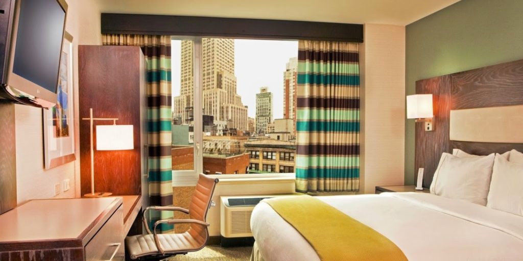a very colorful hotel bedroom with a large window overlooking a city scape on a cloudy day