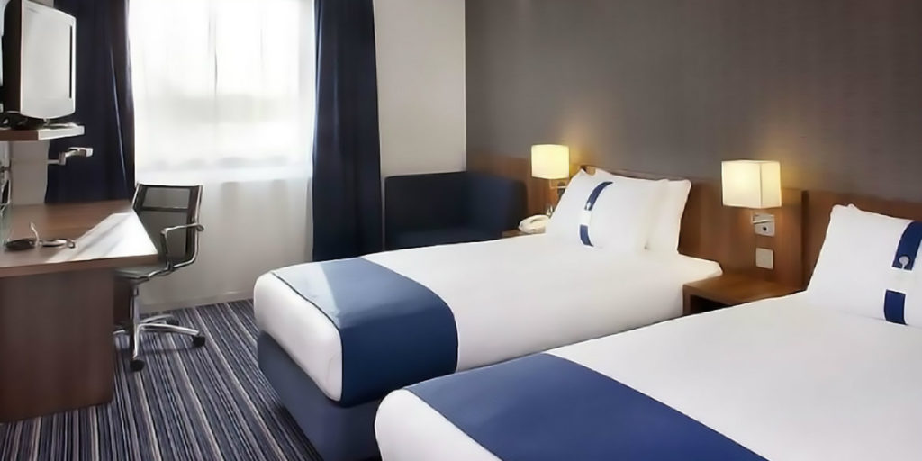 two double beds draped with dark blue and white bedding set on blue gray striped carpet