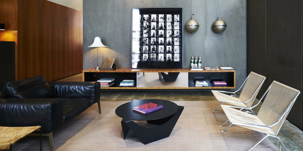 a 70's inspired seating area that includes a large black leather armchair and artistic round black coffee table and two metalic chairs