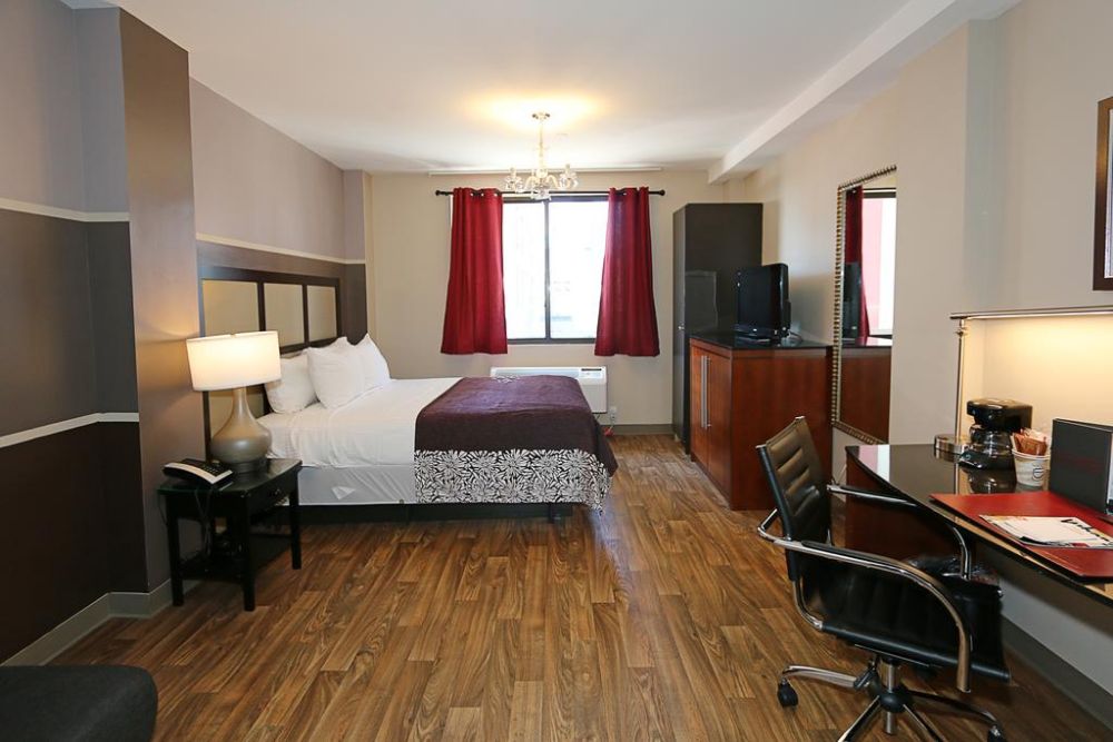 eclectic hotel room with red curtains on the window, queen bed with a plum colored quilt, small desk with office chair