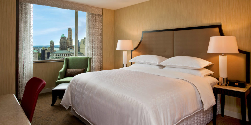 highrise hotel room with classic and elegant bedroom furniture overlooking a city view