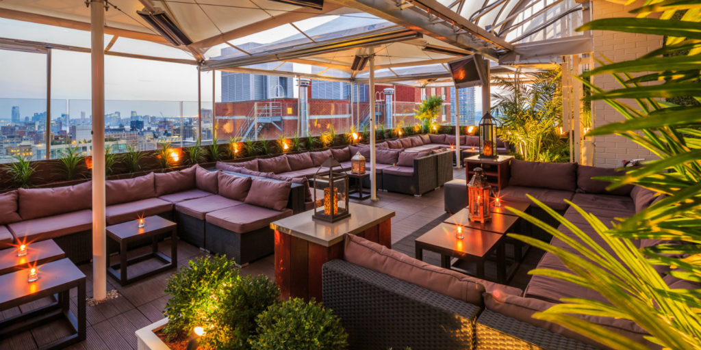 rooftop lounge area overlooking a city at dusk decorated with large purple and black outdoor sectional furniture